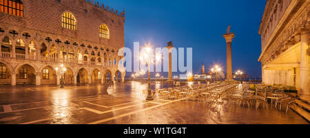 Panorama di Piazza San Marco con la facciata illuminata del Palazzo Ducale, lanterne e colonne con Markus Lion e San Todaro statua in blu Foto Stock