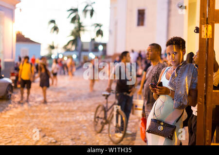 Bella donna cubana sul suo cellulare a terrazze di Trinidad, accanto a la Iglesia Parroquial de la Santisima Trinidad vicino a Plaza Mayor, interne Foto Stock