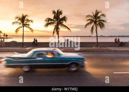 Oldtimer guidando lungo il Malecon di Cienfuegos, punto di incontro di sera e di notte, vita notturna, vuoto street, Palm tree, città coloniale, famiglia Foto Stock