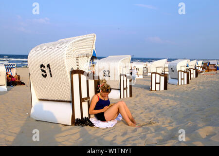 Giovane donna è appoggiata contro una sdraio sulla spiaggia, la lettura di un libro, Strand, Bansin, Usedom, Ostseeküste, Meclenburgo-Pomerania Occidentale, Germania Foto Stock