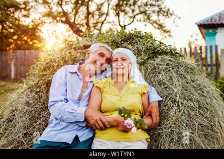 Coppia di famiglia di agricoltori seduti sul pagliaio e rilassante al tramonto in campagna. Duro lavoro di persone avvolgente. Agricoltura e concetto di agricoltura Foto Stock