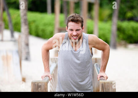 Uomo Fitness cali facendo in palestra esterna allenamento. Atleta maschio facendo forza di formazione sulle barre parallele in Monkey Jungle palestra in spiaggia. Guy esercizio braccia facendo hard esercizi. Foto Stock