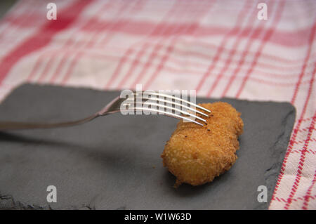 Una crocchetta fatti in casa su una lavagna nera e con una forchetta sulla parte superiore, in background è possibile vedere il rosso tovaglia a scacchi su bianco Foto Stock