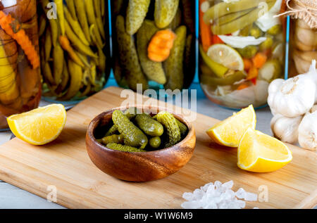 Ciotola di cetrioli sottaceto e vasetti di verdure sott'olio su legno Foto Stock