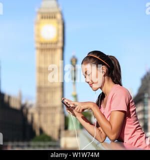 Londra lifestyle fitness donna ascoltando musica in esecuzione playlist sullo smartphone. Appoggio femmina dopo il corso di formazione nella città urbana street. Runner ragazza vicino a Big Ben, Westminster Bridge, London, England, Regno Unito Foto Stock