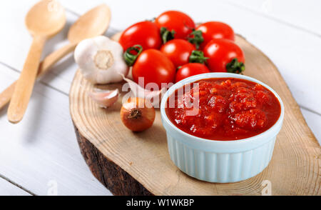 Salsa di pomodoro con aglio, basilico e spezie in una ciotola bianco su sfondo di legno Foto Stock