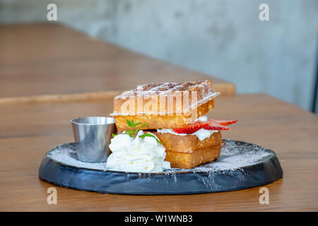 Waffle Strawerry panna fresca nella piastra nera su un tavolo di legno. Foto Stock