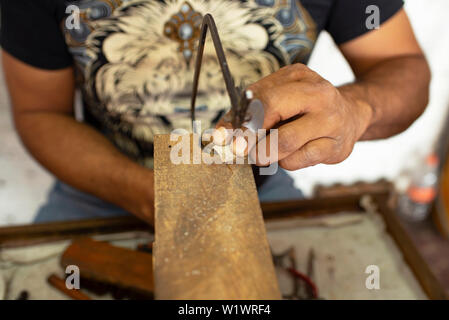 Primo passo per la realizzazione di gioielli: messicana argentiere di taglio piastra di argento con una sega al suo laboratorio di gioielleria in Taxco, Guerrero, Messico. Giu 2019 Foto Stock