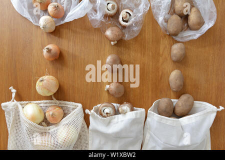 Sottile di plastica riutilizzabile vs cotone sacchetti di generi alimentari con prodotti freschi su sfondo di legno, rifiuti zero concetto. Foto Stock