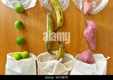 Sottile di plastica riutilizzabile vs cotone sacchetti di generi alimentari con prodotti freschi su sfondo di legno, rifiuti zero concetto. Foto Stock