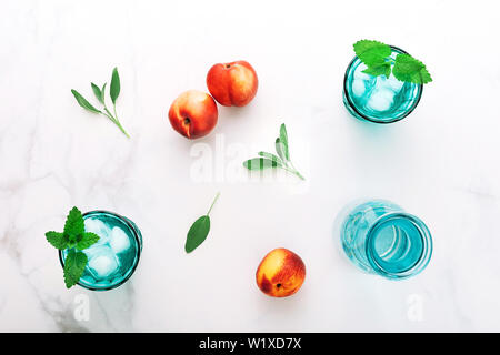 Due belle vintage turchese bicchieri e una bottiglia di bevanda fredda e cubetti di ghiaccio, decorata con fresco verde menta e tre pesche noci a Pentecoste Foto Stock