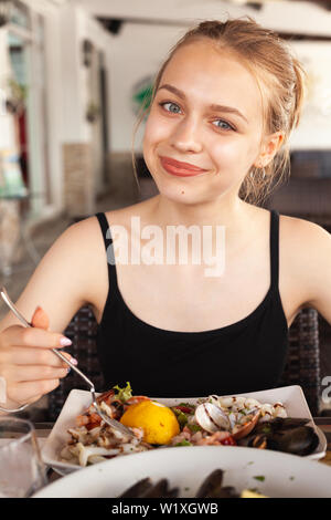 Sorridente bella bionda ragazza caucasica mangia insalate di pesce in un ristorante mediterraneo Foto Stock