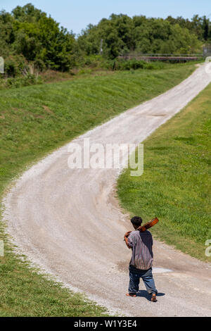 Buras, Louisiana - un afro-americano a piedi nudi uomo che porta una chitarra sulla sua spalla passeggiate lungo una strada di campagna nel sud della Louisiana. Foto Stock