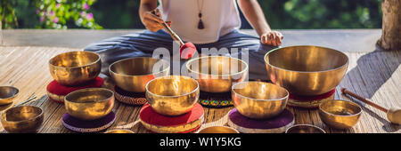 Donna che gioca su Tibetan Singing Bowl mentre è seduto sul materassino yoga contro una cascata. Tonned vintage. Bellissima ragazza con perle di mala meditando BANNER Foto Stock