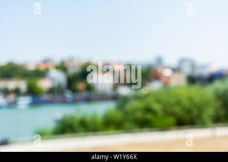 Immagine sfocata di città in riva al fiume per l'altro lato del fiume sfondo background primavera estate parco urbano percorso a piedi accanto alla riva del fiume che scorre attraverso la città Foto Stock