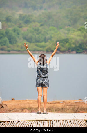 Donne alzando le braccia e sullo sfondo le montagne e acqua al serbatoio Chakrabongse , Prachinburi in Thailandia. Foto Stock