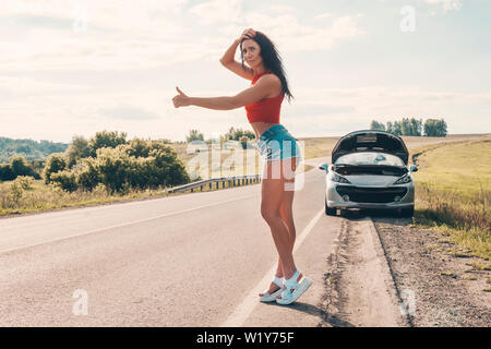 Road Trip, trasporti, viaggi, gesto e concetto di persone felici le giovani donne con broken auto mostra autostop gesto per chiedere aiuto alla campagna Foto Stock