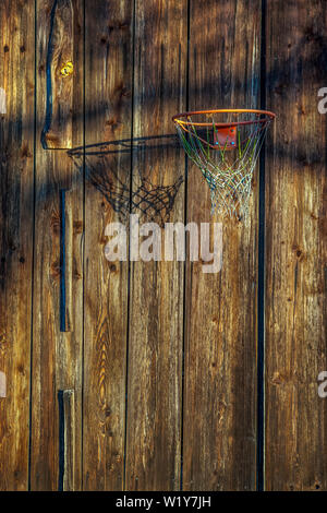 Un vecchio trasandato Basketball hoop sta gettando una serata ombra su un weathered parete in legno Foto Stock