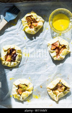 Prugna tartelette sono rivestite o carta di cottura con uovo giallo pronto per essere messo in forno. Foto Stock