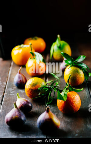 Mandarino Satsuma con foglie su un tavolo in legno con fichi freschi tonalità scura, Foto Stock