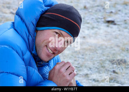 Close up di un maschio alpinista in una spessa down jacket guardando sopra e sorridente alla fotocamera Foto Stock