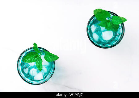 Due belle vintage occhiali turchese con bevanda fredda e cubetti di ghiaccio, decorata con fresco verde menta su marmo bianco tavola. Vista dall'alto. Foto Stock