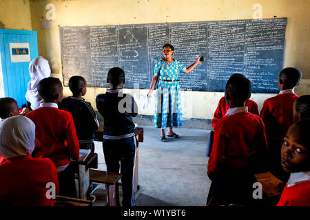 L insegnante e gli studenti in rosso le uniformi scolastiche in una scuola di classe la Mwenge scuola primaria in Mbeya, Tanzania Foto Stock