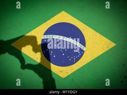 Ombra di mani patriottica messa a forma di cuore nella parte anteriore di una bandiera brasiliana dipinta su un muro di cemento sullo sfondo Foto Stock