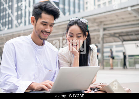 Giovane uomo con ragazza asiatica la riproduzione di laptop sono sorridenti Foto Stock
