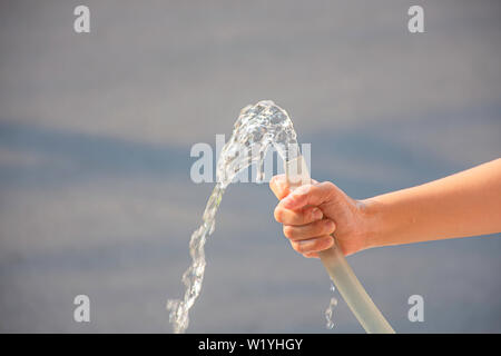 Ragazzo di mano tenendo il tubo di gomma e l'acqua defluisce Foto Stock