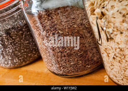 Tre vasi di vetro contenente - Chia semi, i semi di lino (flaxseeds) e avena su un bancone cucina alto. Foto Stock