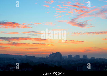 Paesaggio urbano nelle prime ore del mattino: rosa e arancio nuvole su un cielo blu all'alba appena prima del sorgere del sole sopra il pelo sullo sfondo della città Foto Stock
