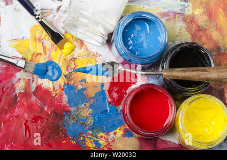 Vasi di vetro con acrilici colori primari e una tavolozza sporca con una spatola e spazzole Foto Stock