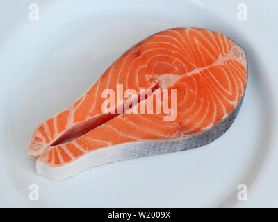 Un pezzo di materie arancione bistecca di salmone con la pelle isolato sul piatto bianco, vista dall'alto. Pesce fresco ingrediente. Foto Stock