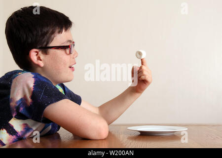 L'esperimento Marshmallow - Bambino seduti ad un tavolo, pazientemente guardando un singolo marshmallow che è posto a stretto contatto nella parte anteriore del bambino la faccia Foto Stock