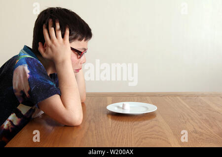 L'esperimento Marshmallow - Bambino seduti ad un tavolo, pazientemente guardando un singolo marshmallow che è posto a stretto contatto nella parte anteriore del bambino la faccia Foto Stock