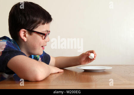 L'esperimento Marshmallow - Bambino seduti ad un tavolo, pazientemente guardando un singolo marshmallow che è posto a stretto contatto nella parte anteriore del bambino la faccia Foto Stock