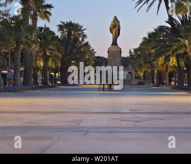 La gente che camminava davanti a Cristo re statua al tramonto accanto alla famosa fontana del Tritone a La Valletta. Foto Stock