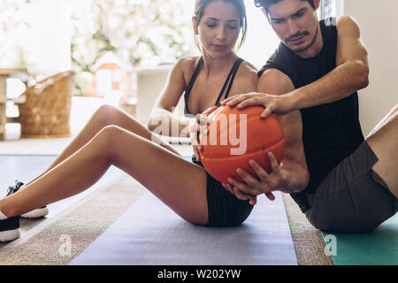 Coppia di fitness a fare gli esercizi con la palla medica a casa. Coppia seduta di schiena su un materassino yoga esercizio facendo passare la palla a vicenda. Foto Stock
