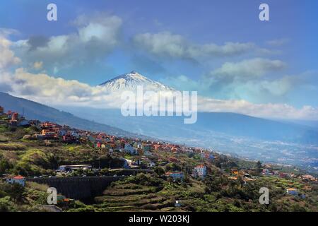 Vista del Teide nevoso, attraverso verdi campi terrazzati del nord di Tenerife e con un cielo azzurro e bianco delle nuvole di luce Foto Stock
