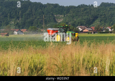 Trattore John Deere con serbatoio rosso nel retro della spruzzatura di un campo Foto Stock