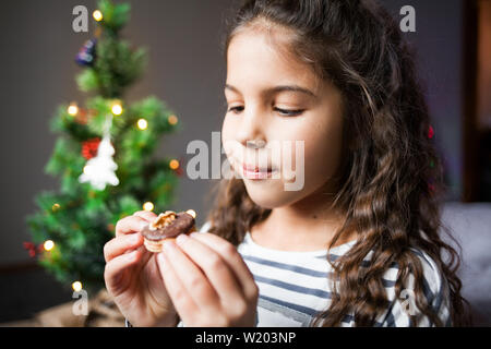 Bambina mangiare biscotti di Natale. Nuovo anno albero sullo sfondo. Foto Stock