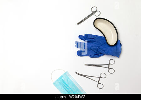 Acciaio inossidabile di grado medico porta ago morsetti, guanti in lattice blu, contenitore metallico su sfondo grigio Foto Stock