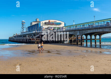 Bournemouth Dorset, Inghilterra, Regno Unito, 4 luglio 2019, meteo: il calore del giorno indugia in prima serata sulla costa sud come un mini ondata di caldo costruisce. Due giovani donne correre lungo la spiaggia vicino al molo nel calore estivo. Credito: Paolo Biggins/Alamy Live Foto Stock