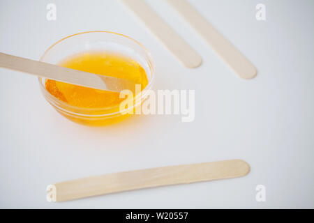 Ceratura. Pasta per addolcire in un salone di bellezza. Concetto di depilazione con cera e bastoni su sfondo bianco vista superiore Foto Stock