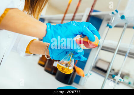 La donna o mani femminili in guanti protettivi tenere il tubo di prova nelle mani di chimica produce esperimento di test e la ricerca in un moderno laboratorio di chimica. Foto Stock
