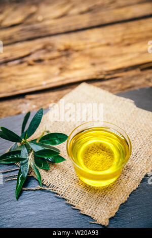 Organico, sana e naturale pressato a freddo Olio di oliva su un tavolo di legno. Virgin italiano o spagnolo di olio di oliva in una ciotola per una sana prima colazione Foto Stock