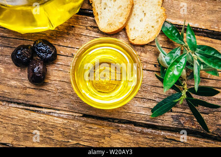 Organico, sana e naturale pressato a freddo Olio di oliva su un tavolo di legno. Virgin italiano o spagnolo di olio di oliva in una ciotola per una sana prima colazione Foto Stock