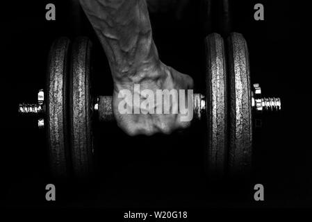 Una mano saldamente la presa di 22kg dumbbell rivelando bulboso vene del dorso della mano e polso. Nessuna ovvia branding. Foto Stock