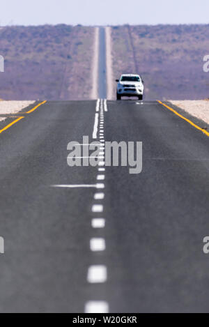 White Toyoya Hilux pick-up truck guidando lungo una retta molto e a lungo su strada asfaltata attraverso il deserto del Kalahari, Namibia Foto Stock